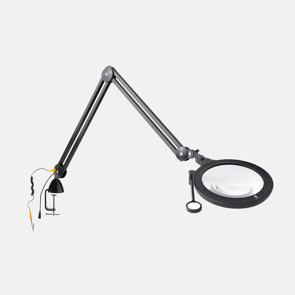 A black adjustable desktop magnifier lamp with a circular magnifying glass, hanging loop, and separate clamp lamp attachment on a light gray background.