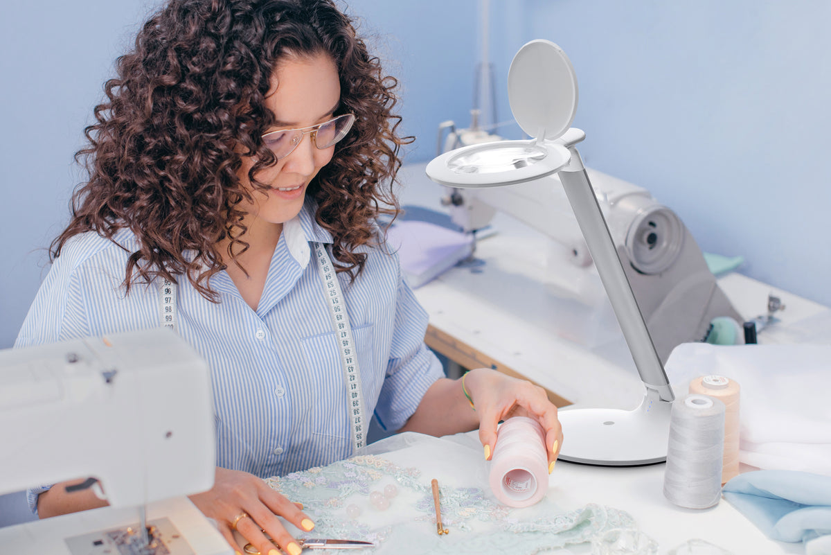 Woman with glasses working at a sewing machine with Halo lamp positioned above material. 