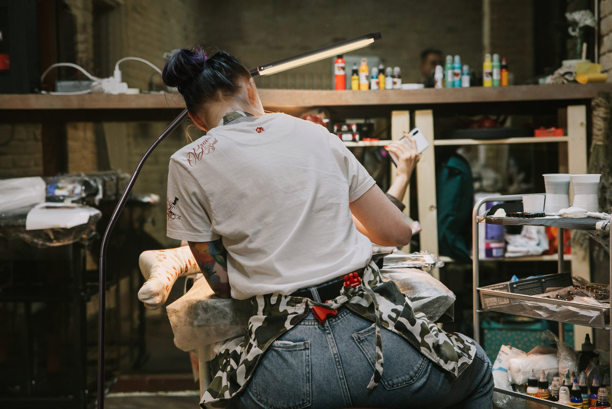 Person in craft studio with various equipment and supplies. Light is bent over work space. 