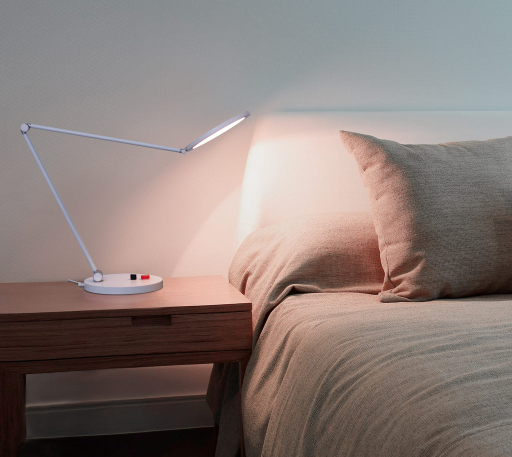 Foldable arm desk lamp on a nightstand next to a bed with beige bedding.