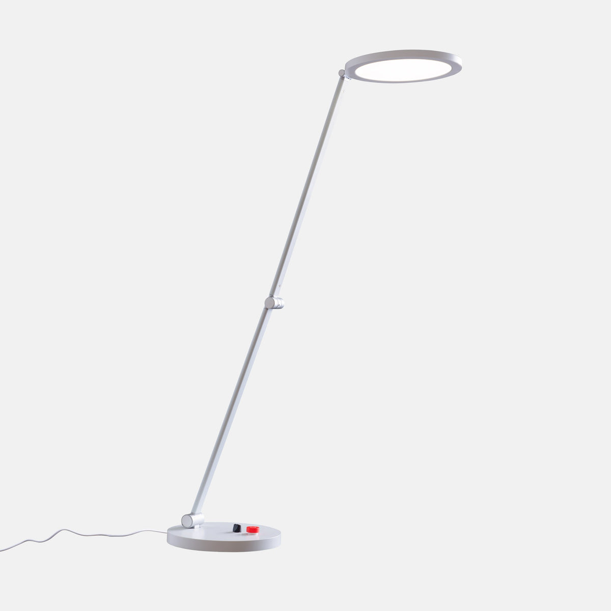 A modern adjustable lamp with a thin silver metal stand, a circular ring-shaped head, and a small red and black switch on the base, shown against a light gray background.