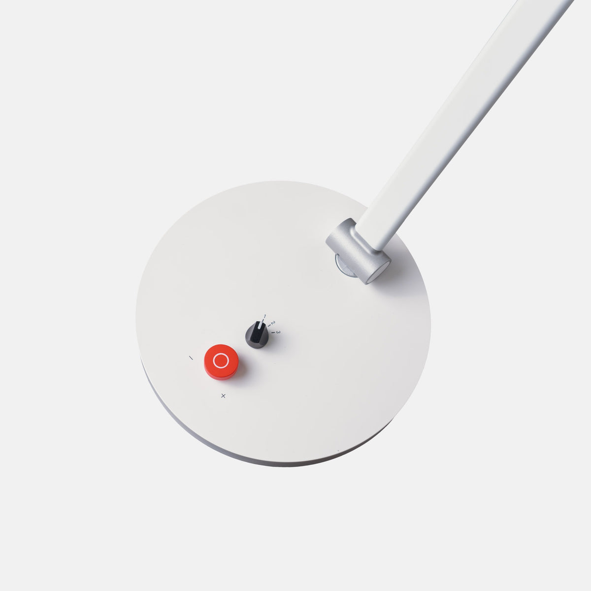 A close-up of a modern white desk lamp showing its circular base, adjustable arm, and a small red power button with a white ring on top.