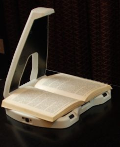 LyriQ book reader holding an open book, shown on a dark reflective surface against a dark patterned background.
