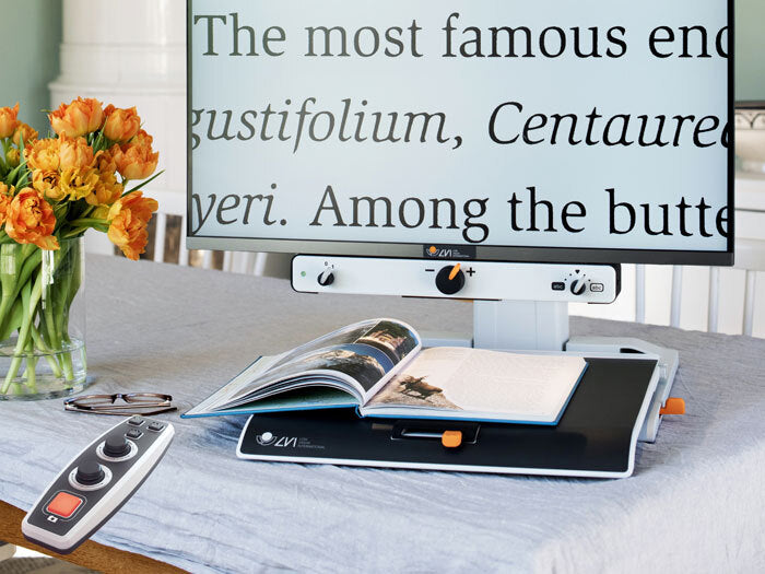 MagniLink on a table being used to read a magazine. Remote control is in the foreground. 