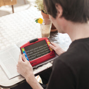 Person using a RUBY 7 HD device to magnify text from a magazine