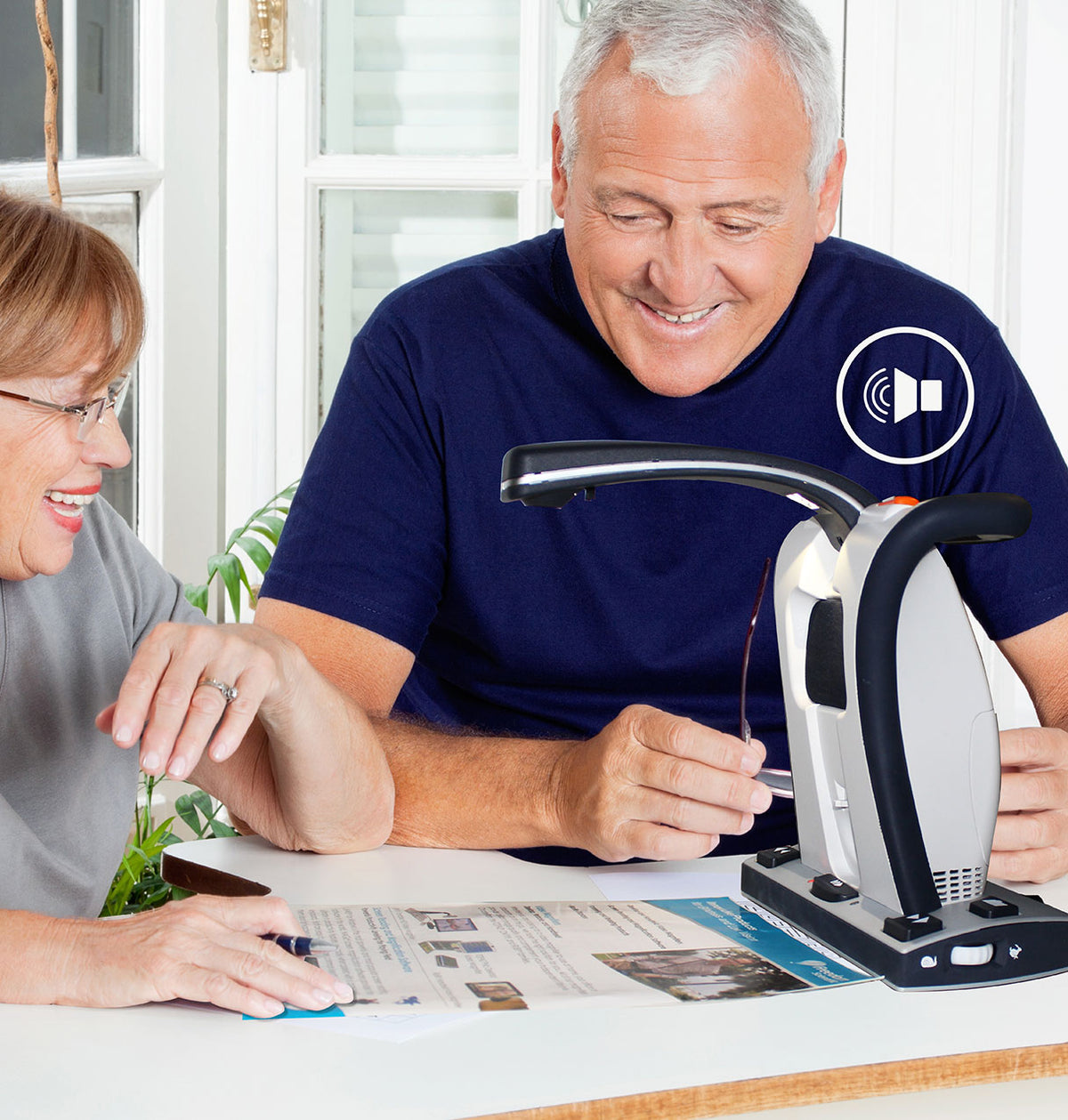 Two people using a Smart Reader HD magnifying device at a table to read a brochure