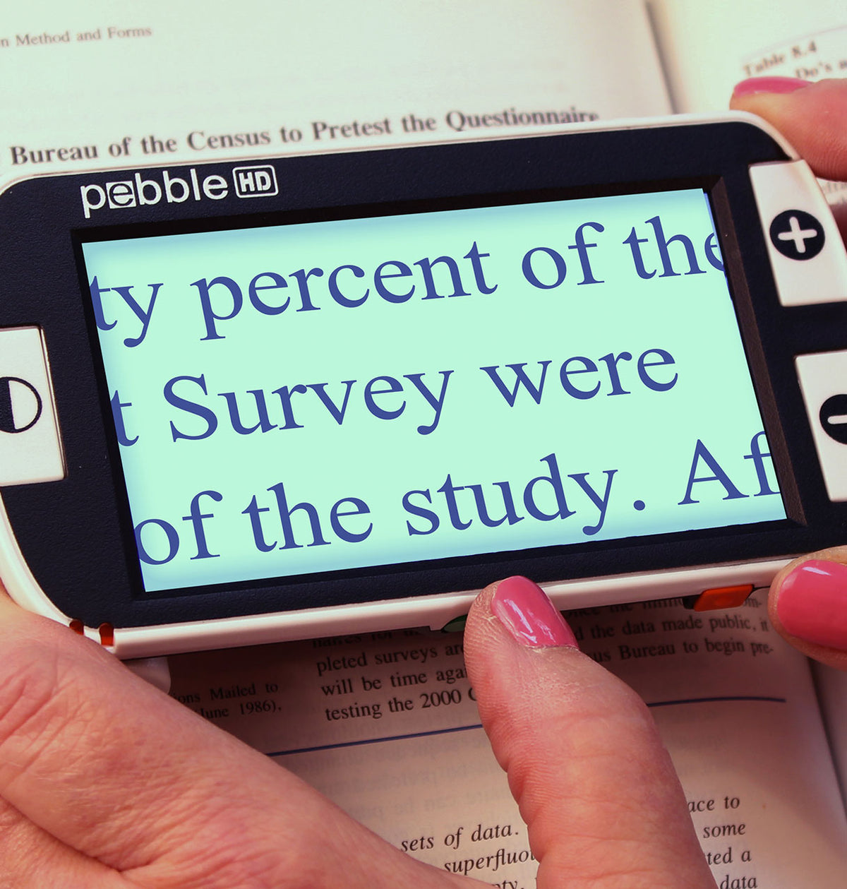 Pebble HD device held over a book with text displayed on its screen.